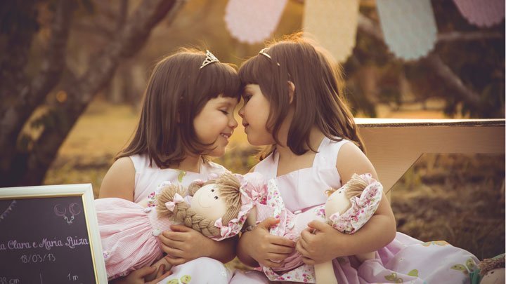 identical twin girls holding twin dolls