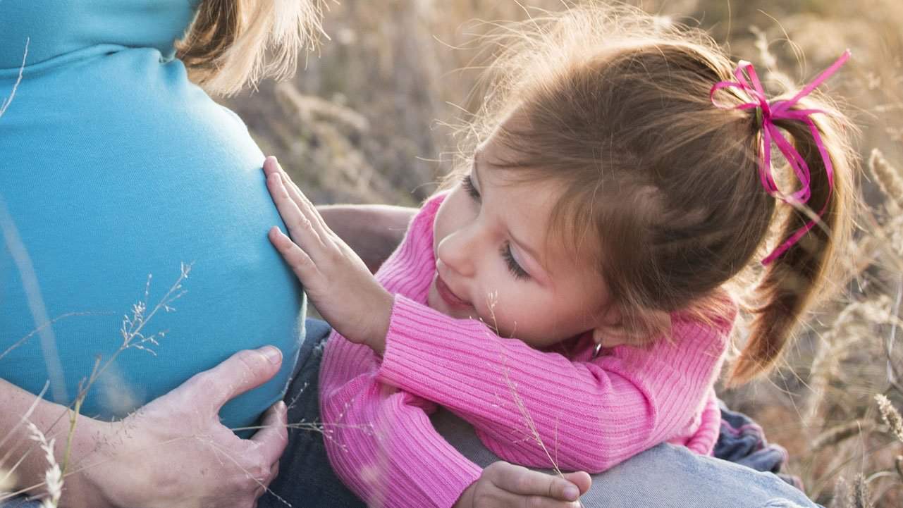 Young daughter touching mothers twin pregnancy belly